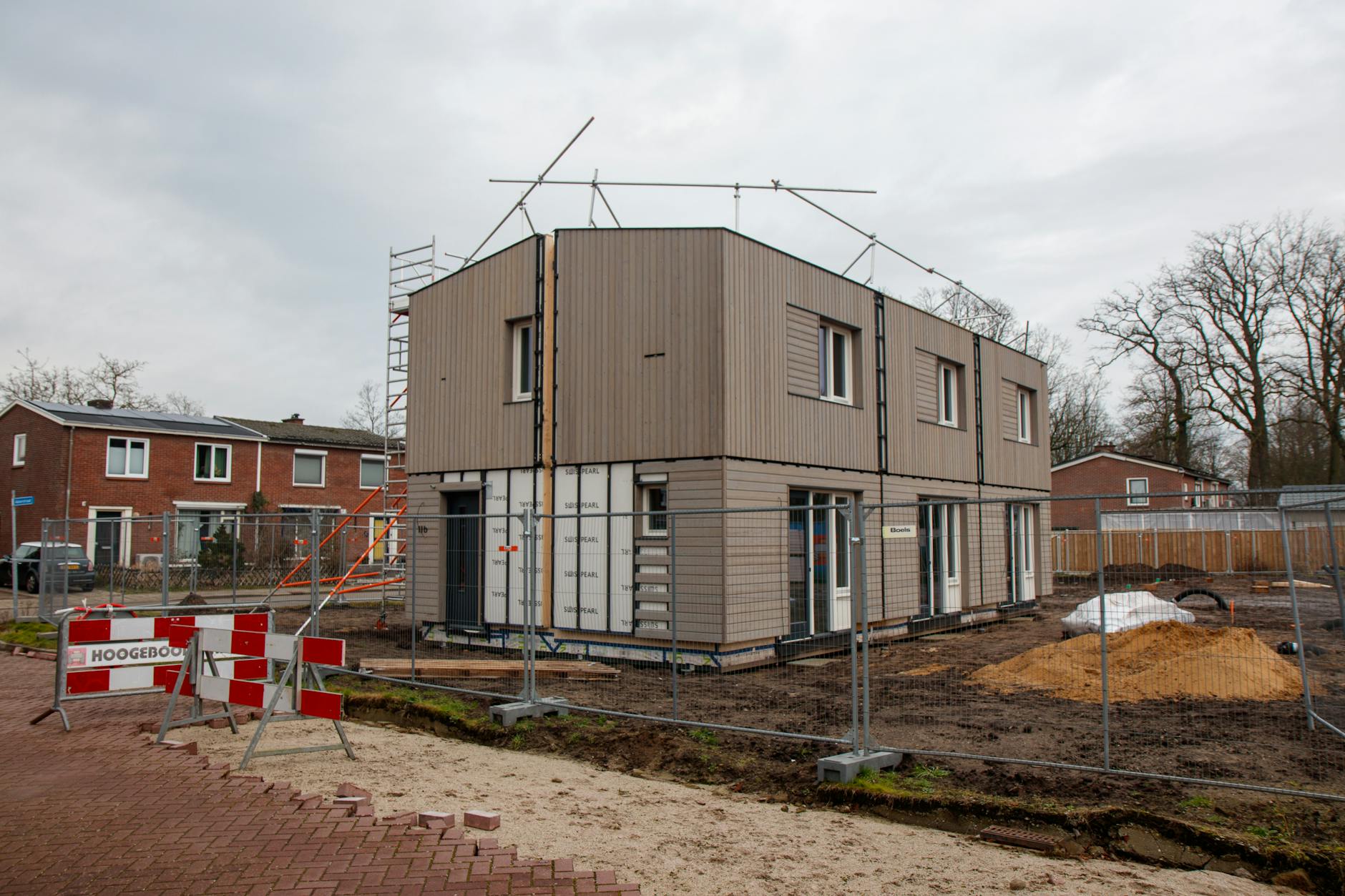 Newly built two-storey house with grey cladding surrounded by construction fencing on an overcast day