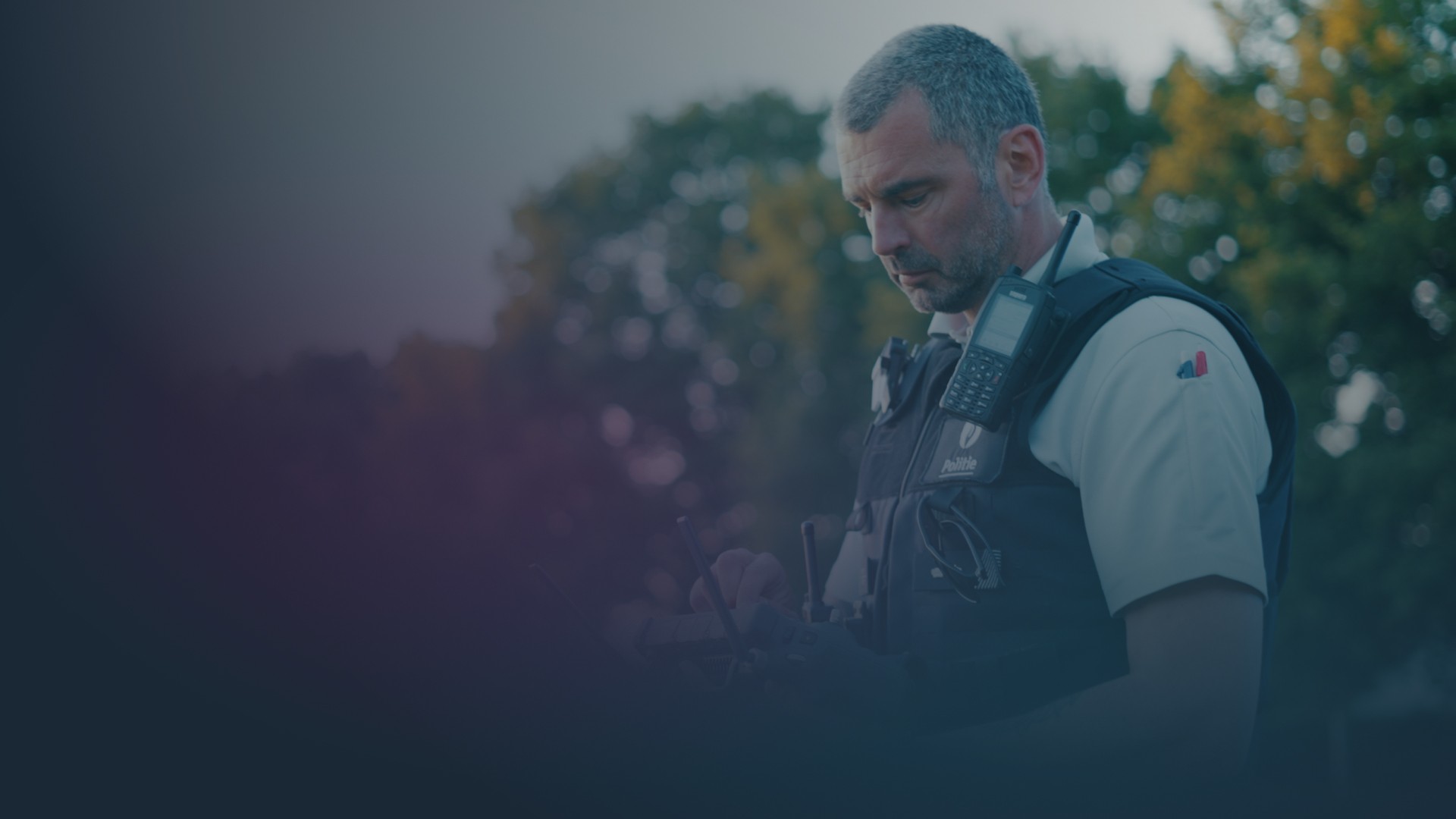 Ein Drohnenpilot der Polizei steht im Freien und hält einen Fernsteuerungscontroller mit angebrachtem Tablet, während er sich auf den Bildschirm des Controllers konzentriert, um eine professionelle Drohne während einer kritischen Mission zu steuern.
