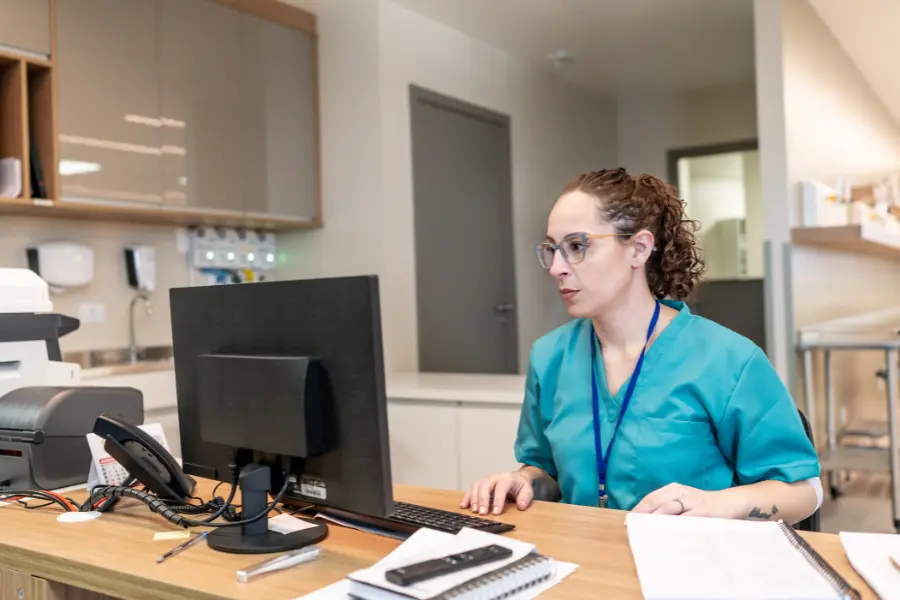 AI pharmacy solutions represented by a nurse managing digital records at a clinic reception desk with prescription tools nearby.
