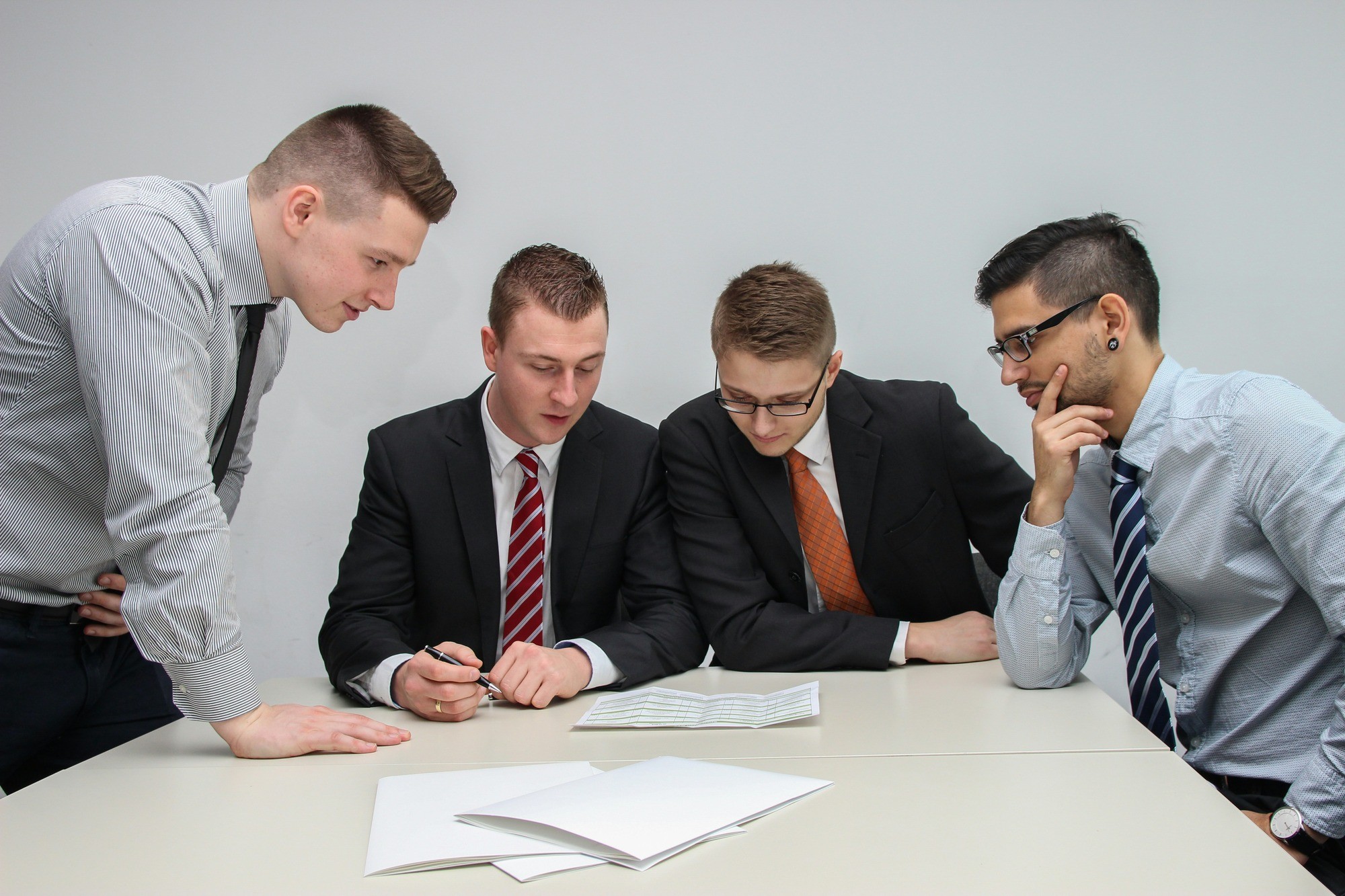 Four men in business attire gather around a table, engaged in discussion while reviewing documents.