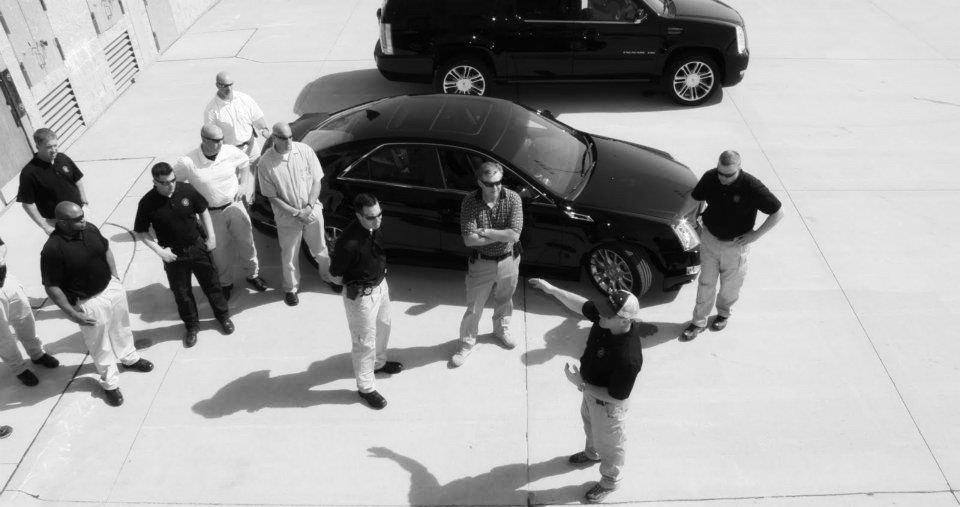 Black and white photo of 9 trainees paying attention to the intructions coming from the close protection trainer.