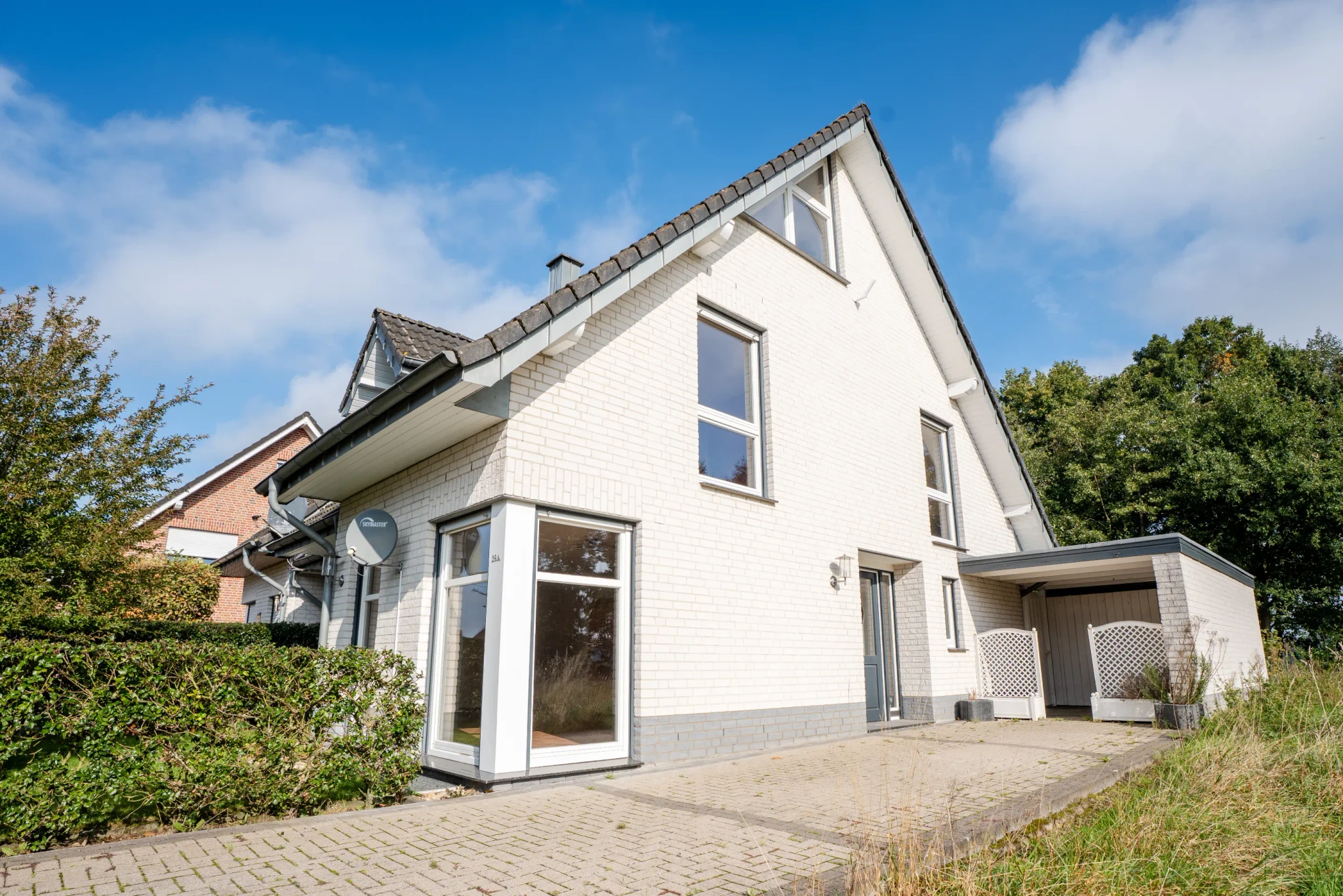 Moderne Doppelhaushälfte mit heller Klinkerfassade und Carport in Heek-Nienborg, präsentiert von Westfalen Wohnen.