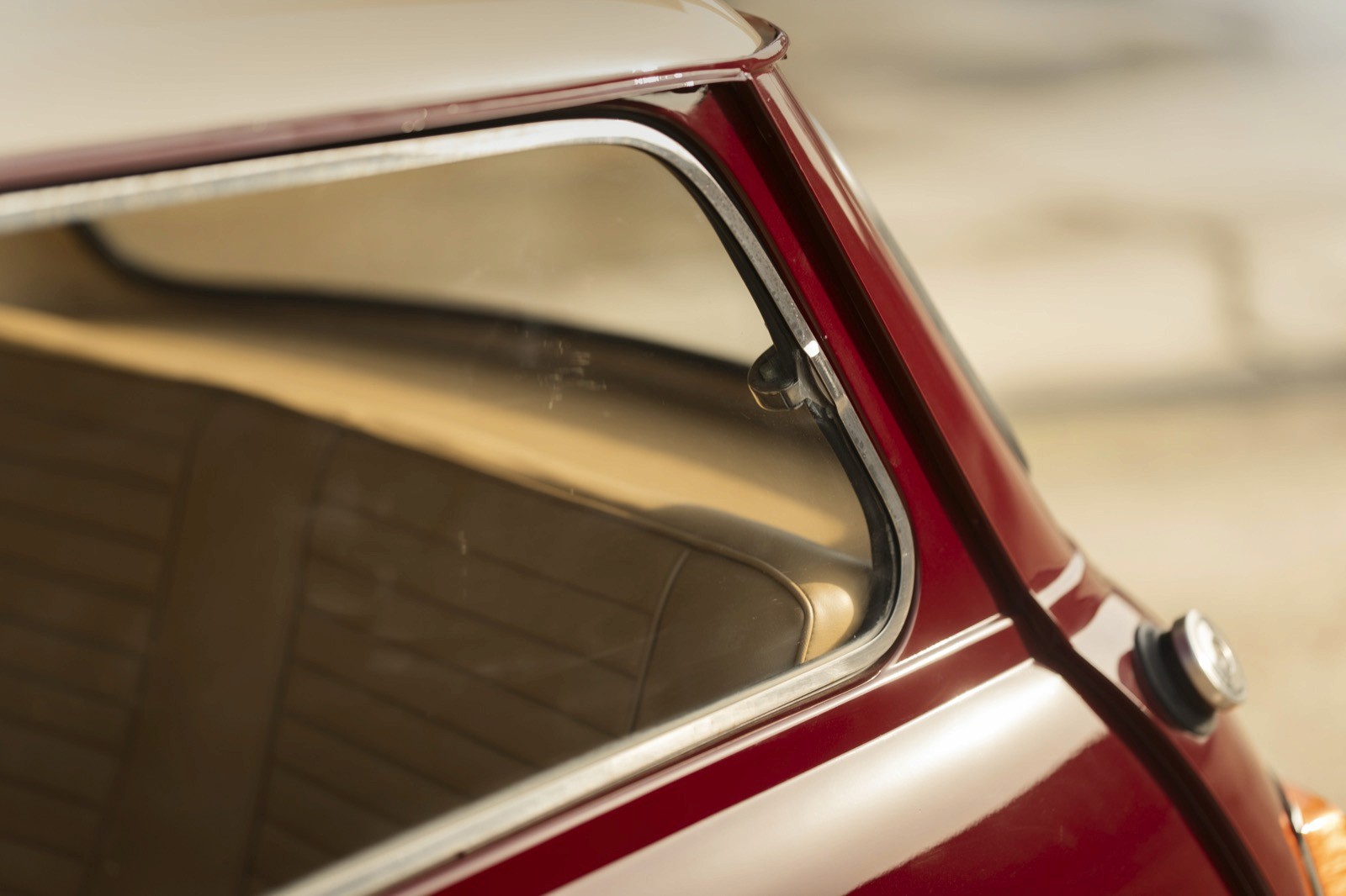 Close-up of a vintage car window with a shiny frame and a soft, beige interior visible through the opening.