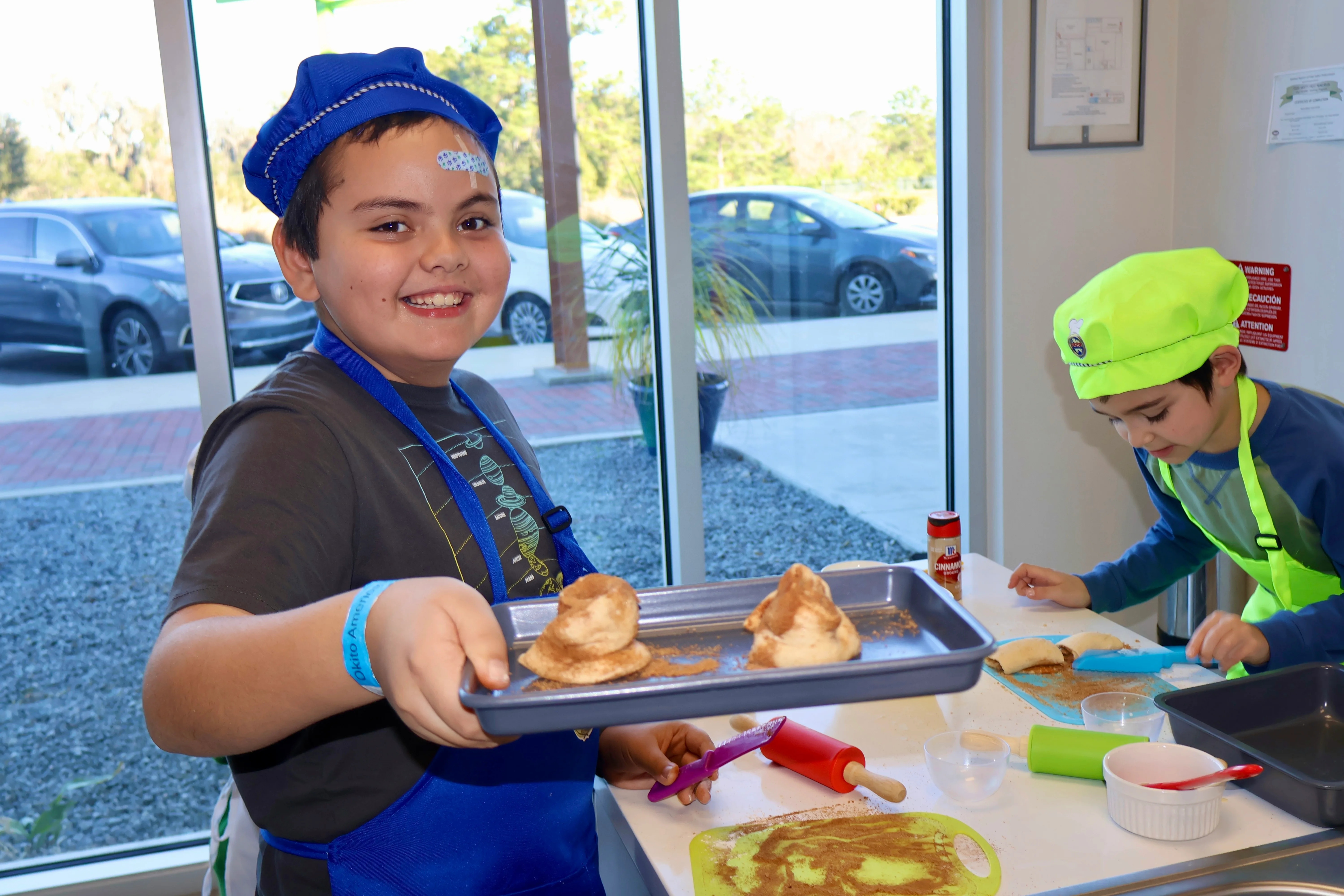 A smiling child holding up a tray with cinnamun rolls ready to bake