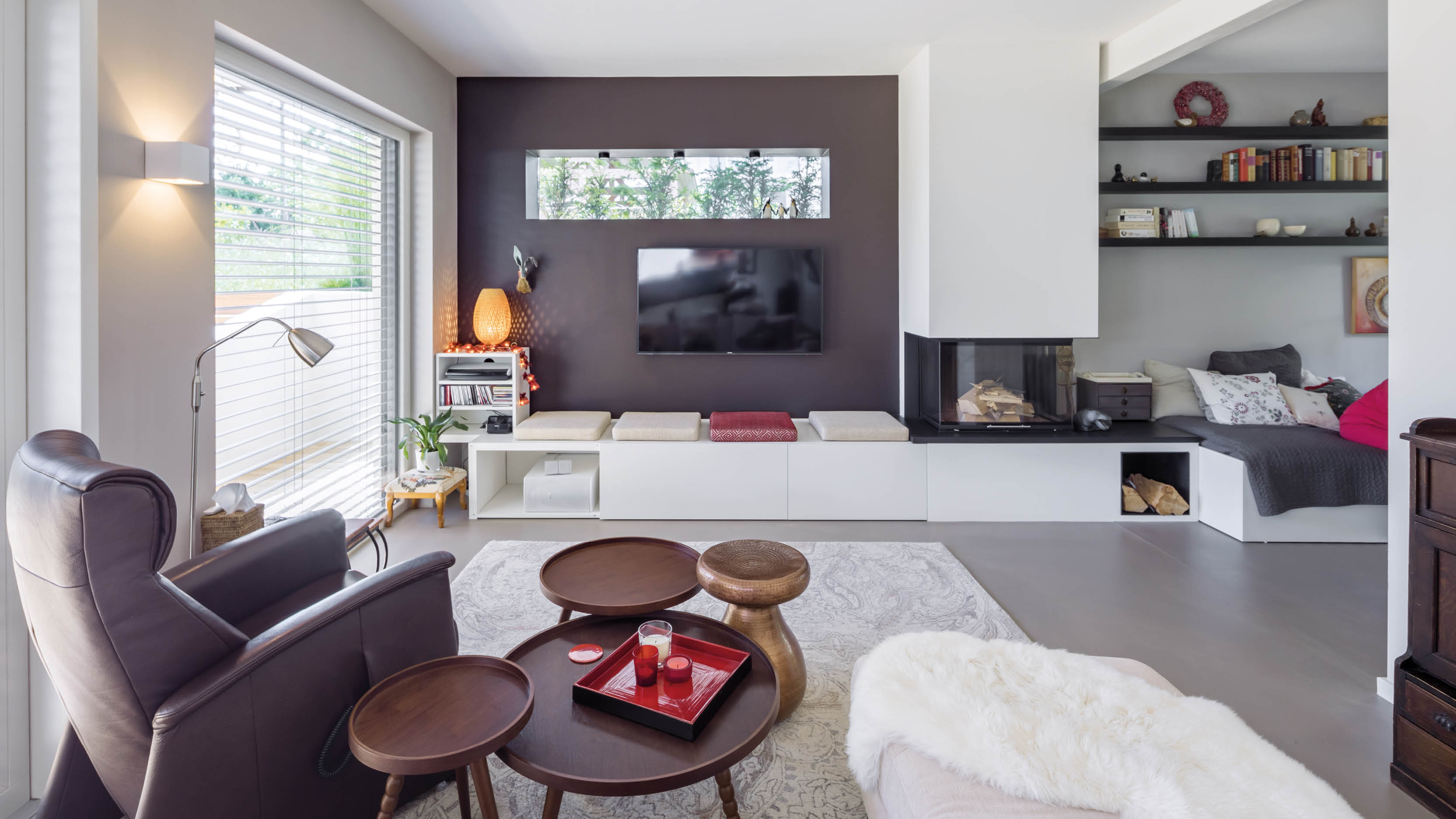 Modernes Wohnzimmer mit Ledersessel, Kamin, Fernseher und Bücherregalen, dekoriert mit Kissen und einer Fell-Decke.