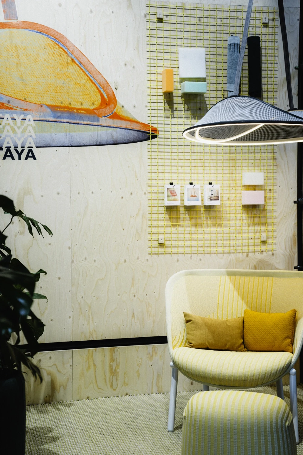 Yellow striped armchair with cushions under a pendant light in front of plywood walls with material samples.