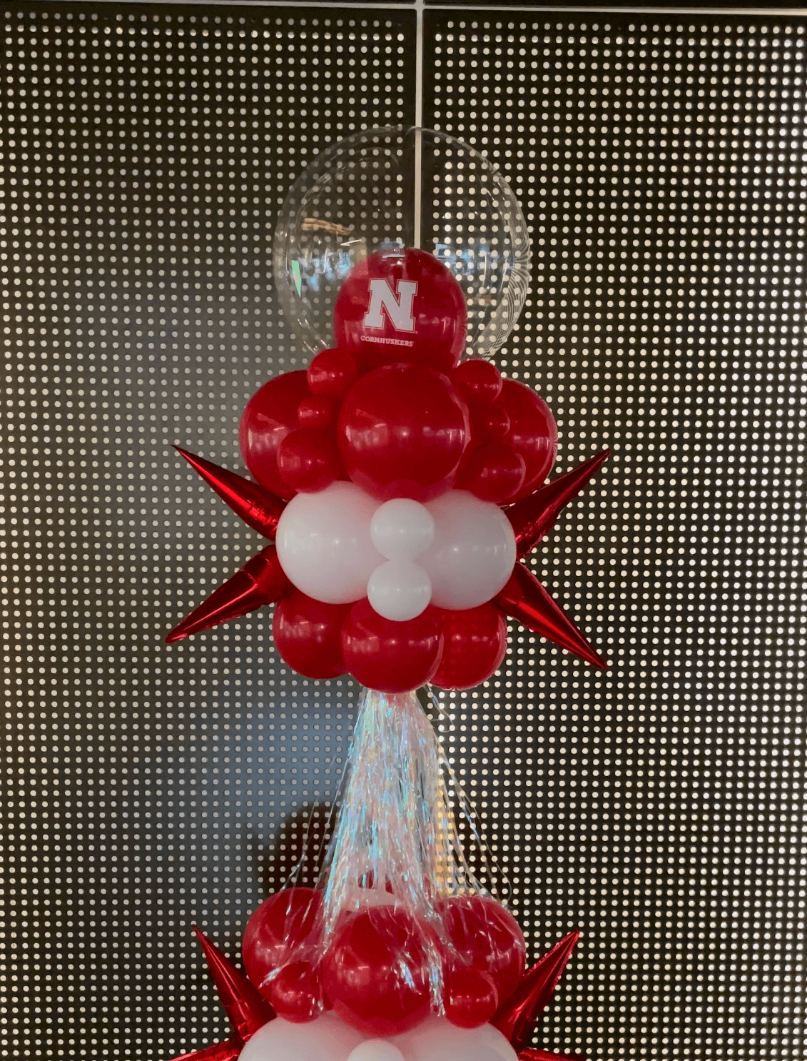 University-themed balloon column in red and white, featuring a large “N” balloon topper, with star-shaped accents and a metallic finish, perfect for sports events or university celebrations. Susa’s Sweets & Balloons.