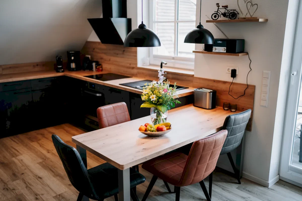 Moderne Küche mit Tisch, Stühlen und Blumenstrauß. Schwarze Schränke und Holzboden für ein gemütliches Ambiente.