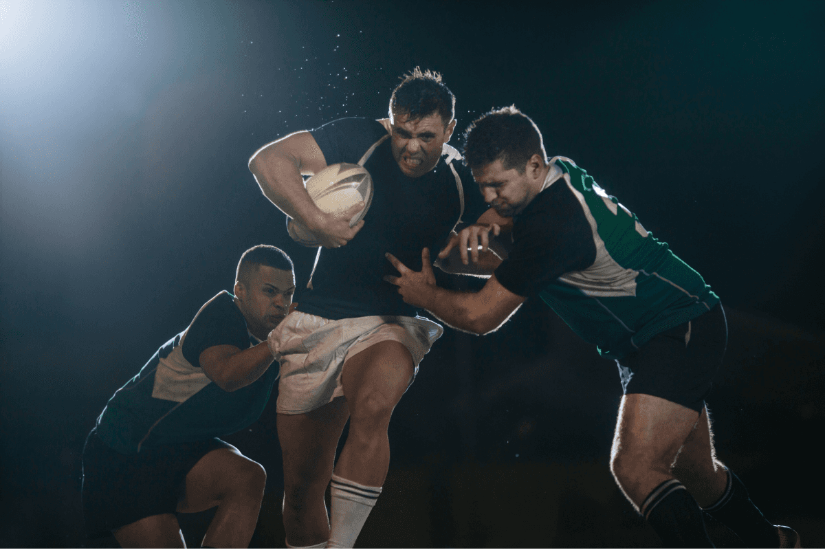 Rugby players contesting the ball during a floodlit club match tackle