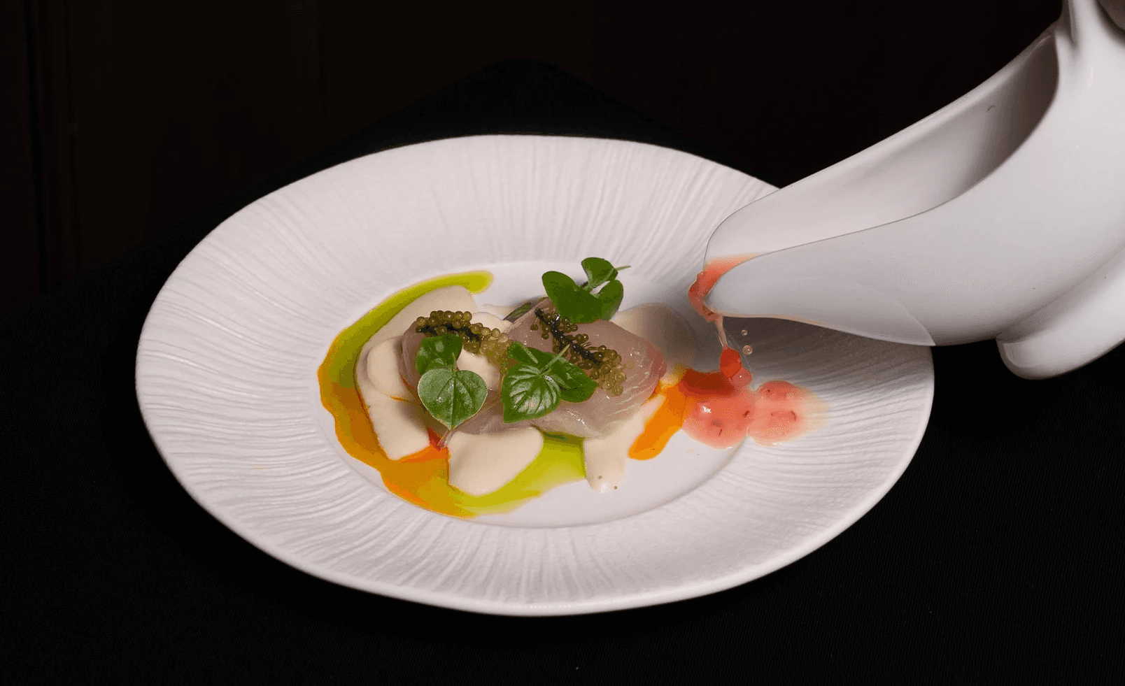 White plate with roasted chicken served in a golden sauce with herbs and capers, placed on a terrazzo tabletop in sunlight.