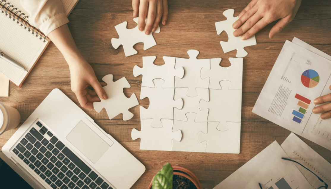 Hands assembling puzzle pieces, illustrating The Raising Collective bringing the missing piece to your brand.