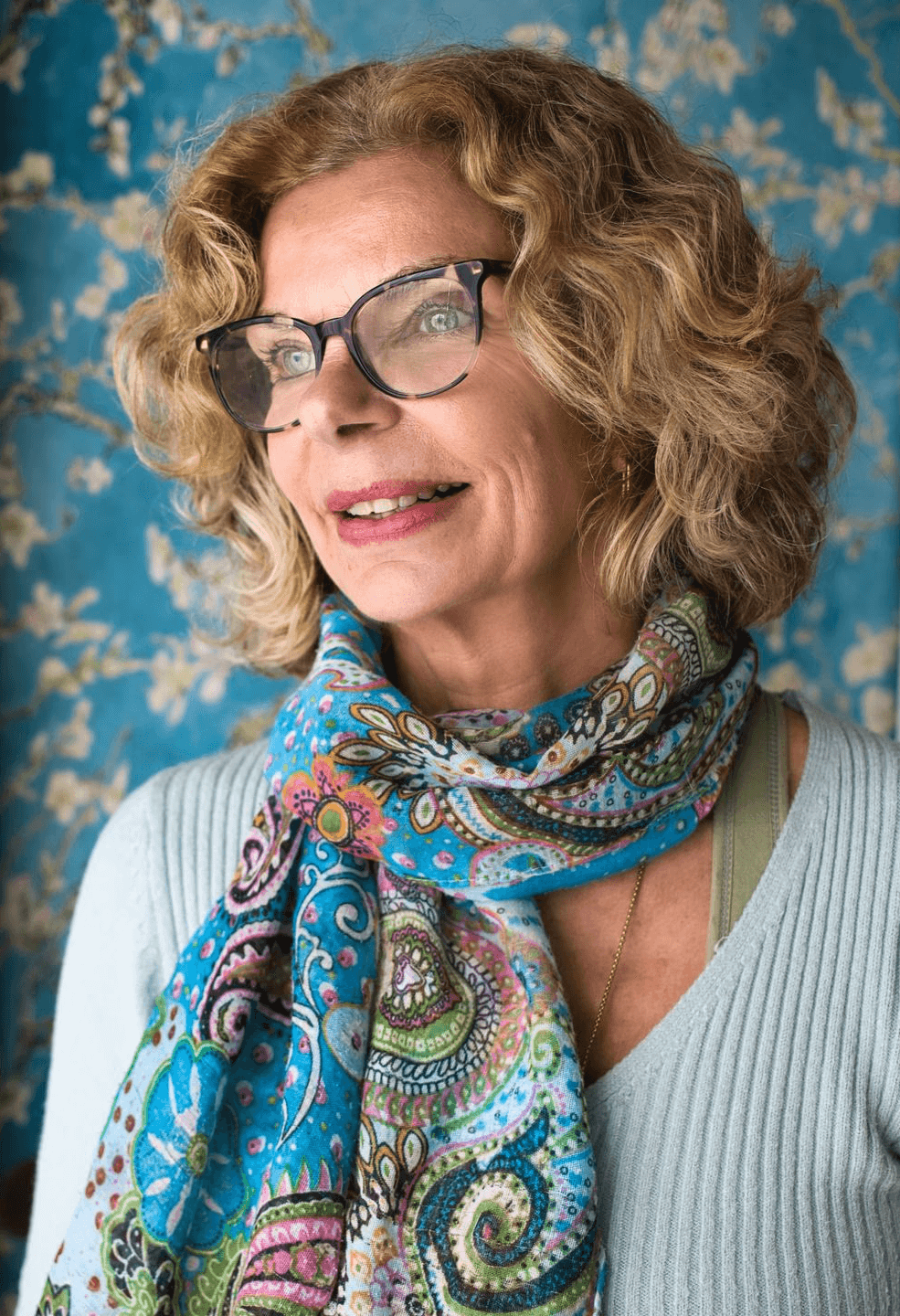 A woman sits cross-legged with eyes closed, wearing a white blouse and a long purple skirt, looking serene.