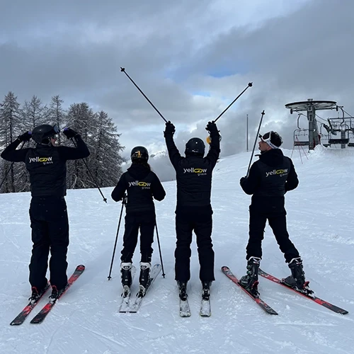 Quatre skieurs de Yellow Glass en tenue noire, avec des bâtons, posent sur une piste enneigée.