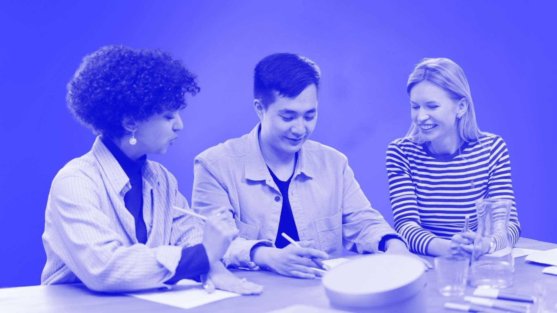 3 people sitting at a table looking at a piece of paper, two of whom with pens in their hand