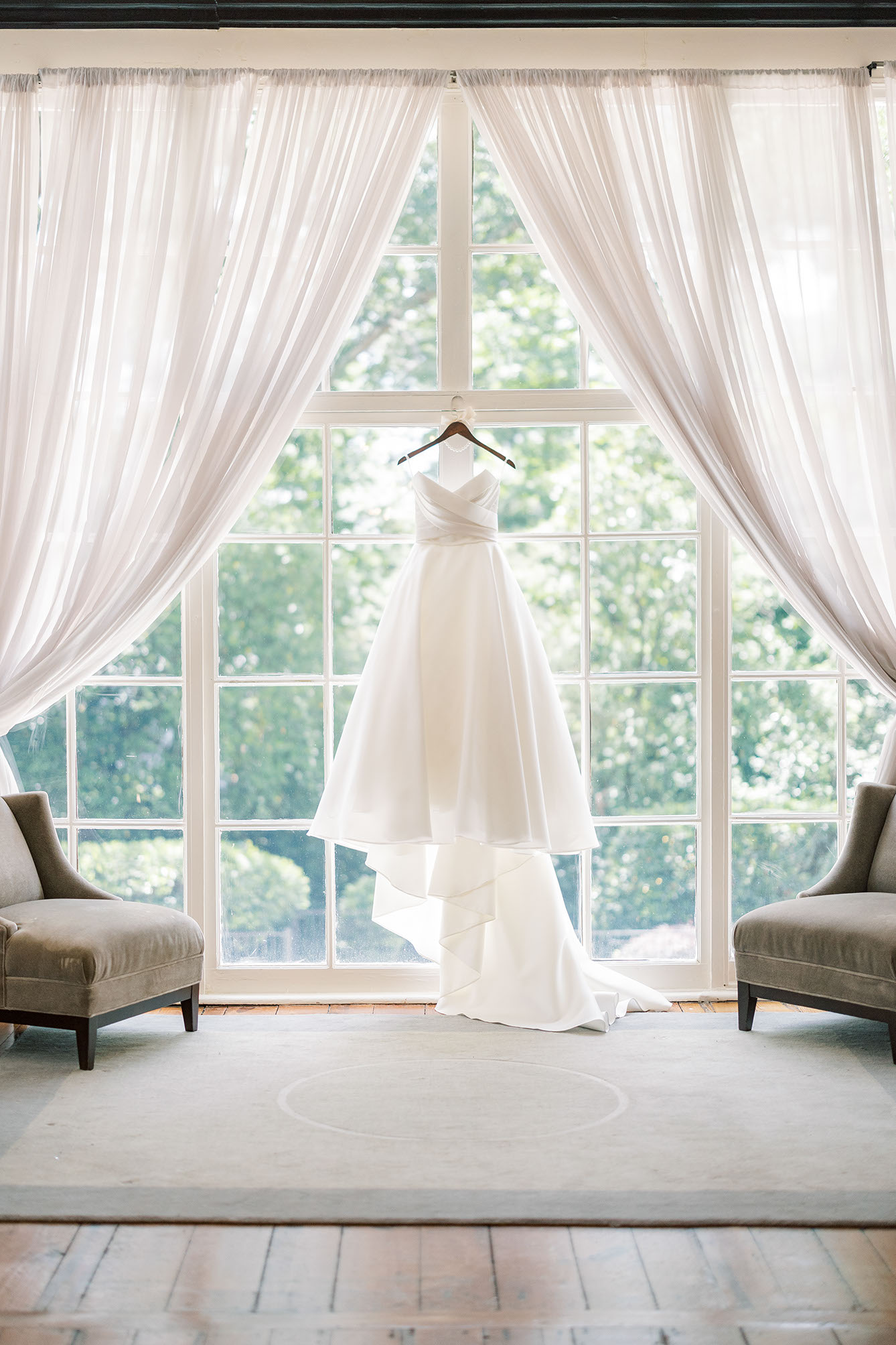 Wedding gown hanging in a sunlit arched window before the ceremony.