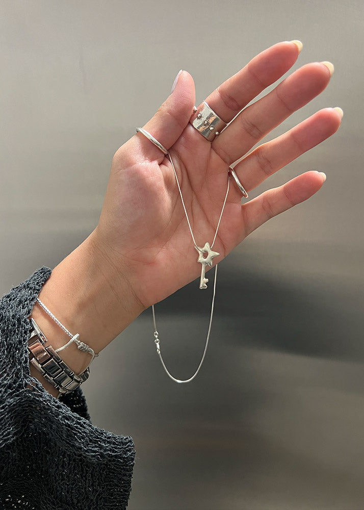 Hand holding a silver necklace with a star pendant against a neutral background