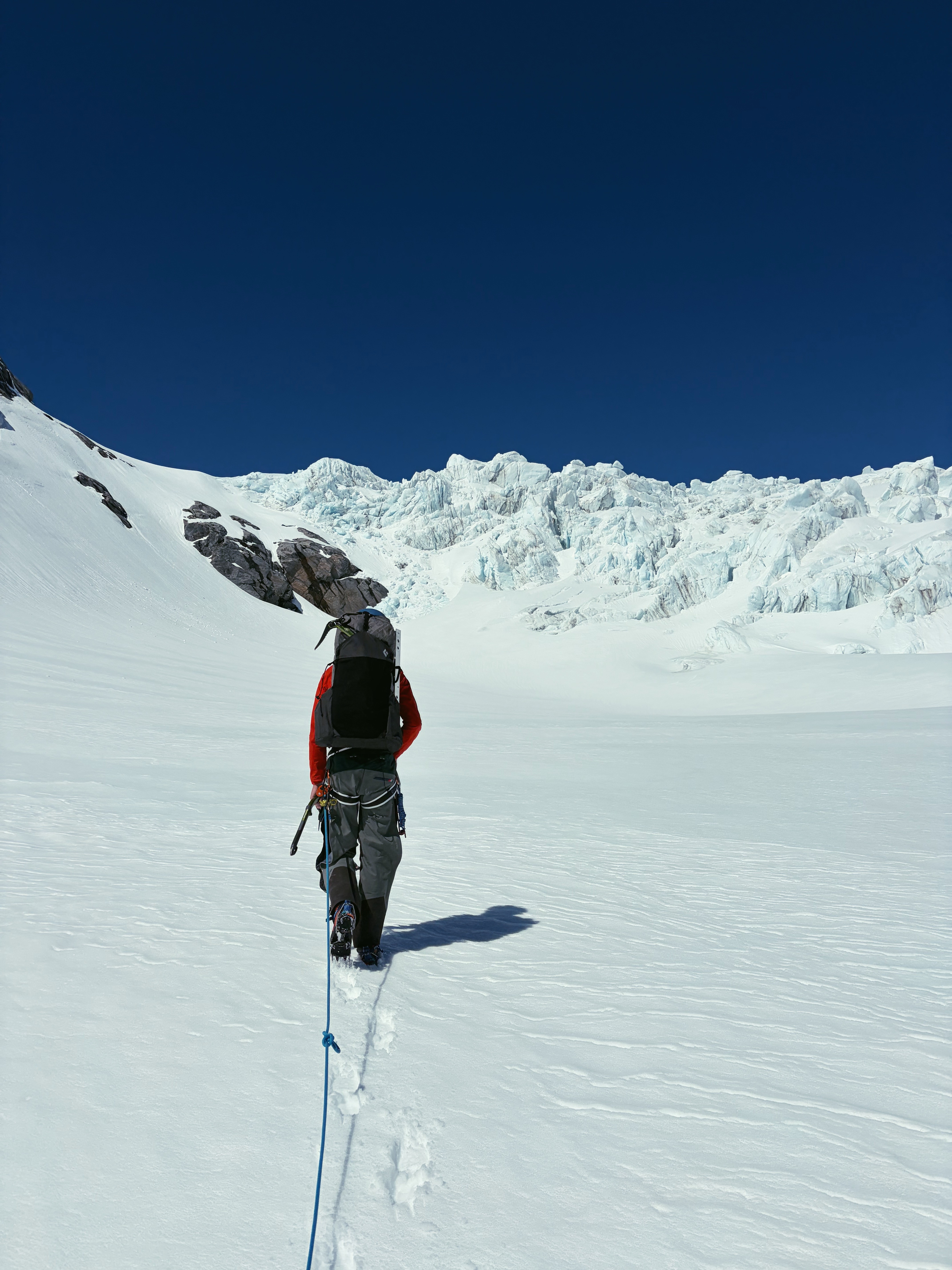 A roped climber crossing a sunlit glacier below broken ice