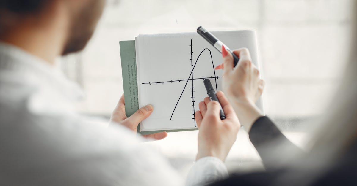 Two professionals discussing a parabola graph on a notebook, promoting teamwork and collaboration.