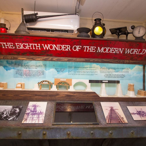 Exhibit displaying historical bridge models and photos under a sign reading "THE EIGHTH WONDER OF THE MODERN WORLD."