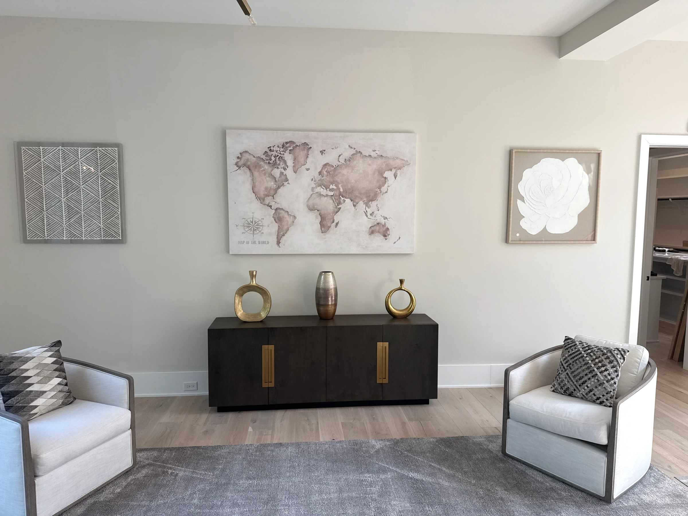 Map artwork and smaller pieces above a sideboard between lounge chairs.