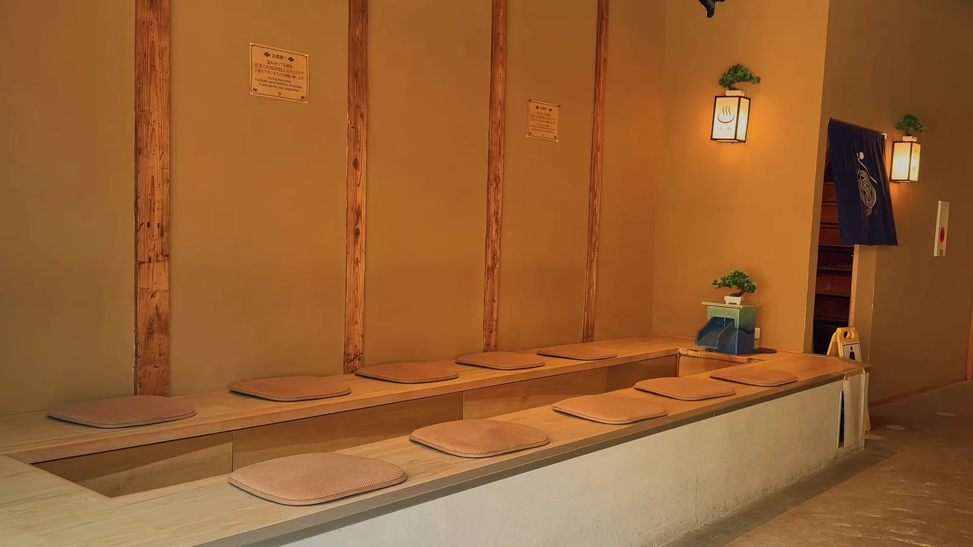 A row of raised tatami platforms along a plaster wall in a Kinosaki bathhouse changing room.
