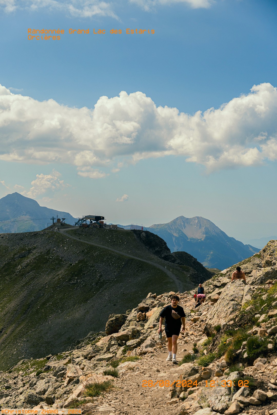 Randonneur en montée sur un sentier rocailleux avec vue sur les montagnes.