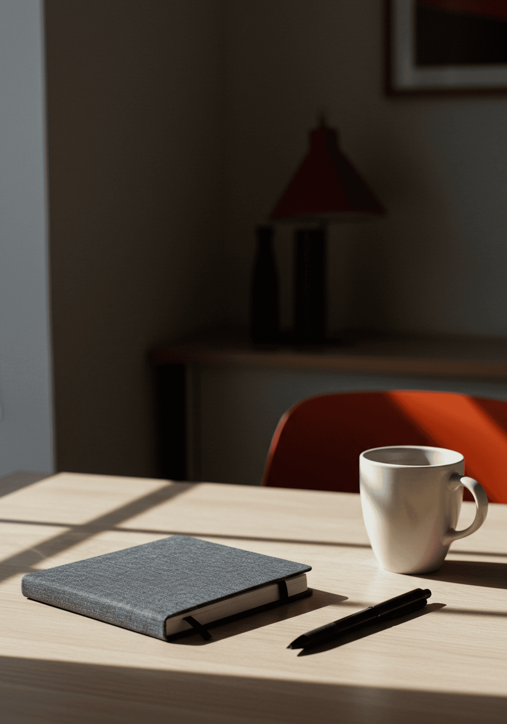 Minimalist desk setup with a gray notebook, black pen, and white mug, bathed in natural light. Perfect for productivity inspiration.