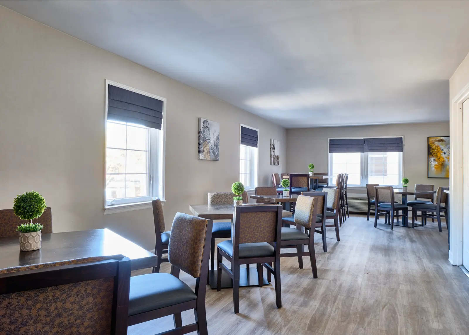 Dining room with tables and chairs arranged for socializing, featuring decorative plants and wall art.