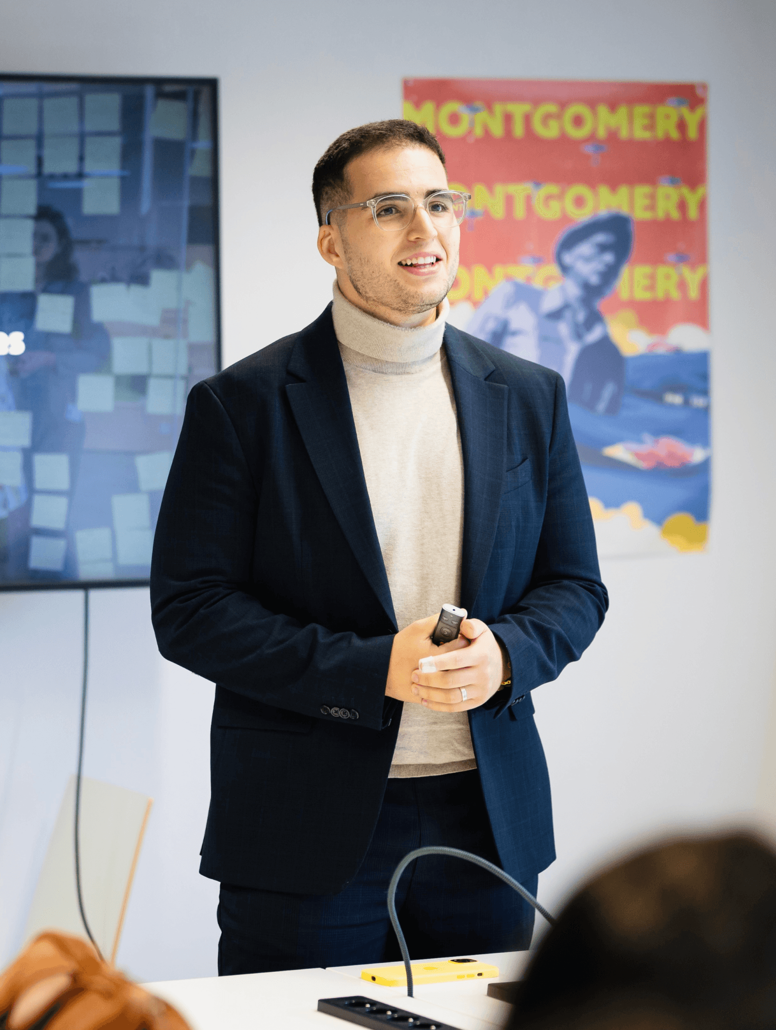 Facilitator leading a workshop session in a modern meeting room, with sticky notes on the screen and a Montgomery poster in the background