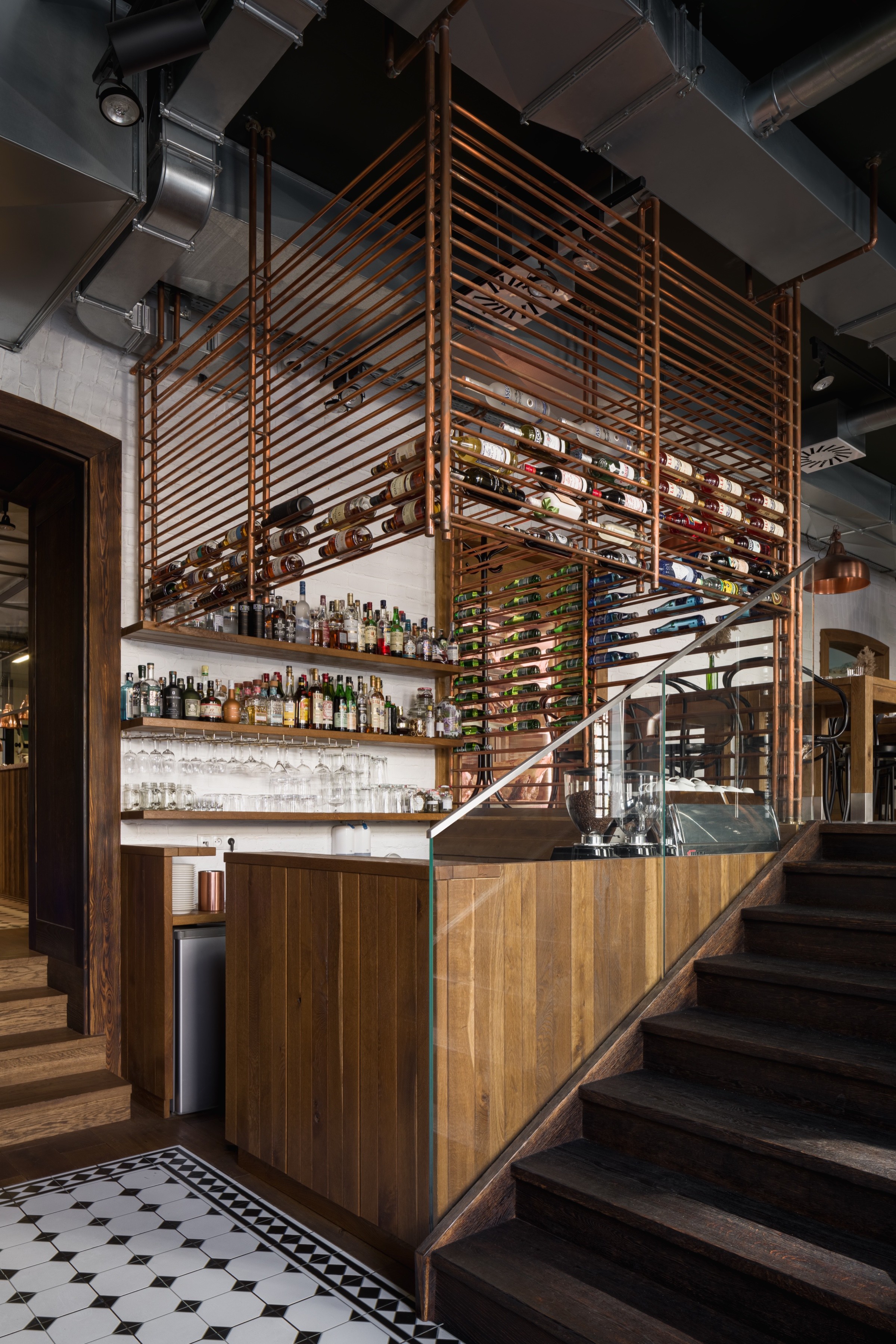 Bar z drewnianą ekspozycją butelek i schodami nad posadzką z mozaiki - The Farm