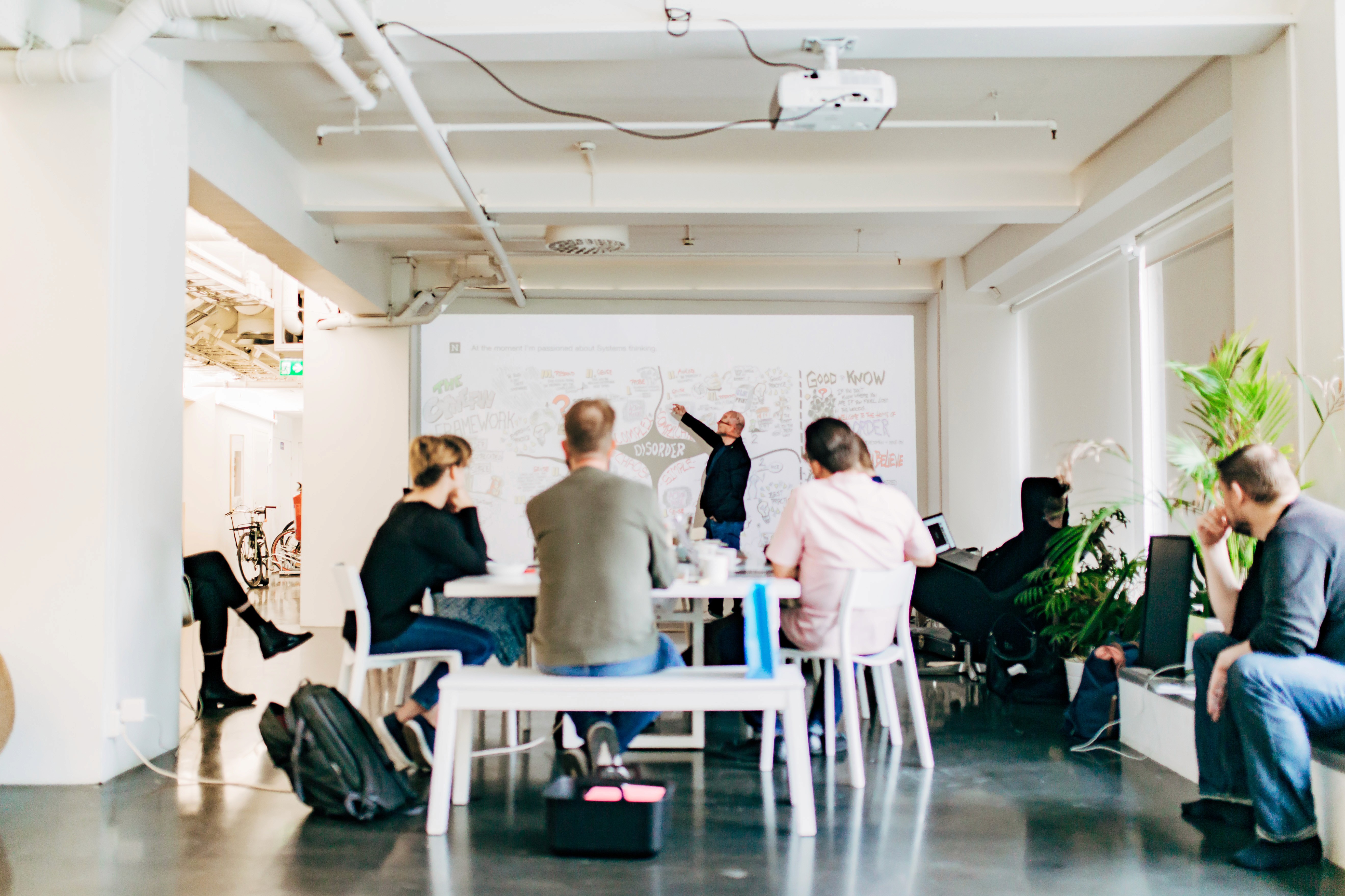 Black and white image of people working at a table with laptops, showing hands gesturing during discussion of digital content displayed on screens, with fabrica® logo in the corner.