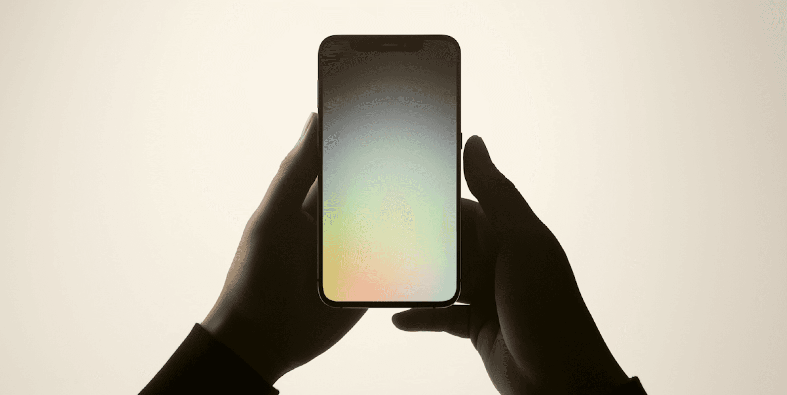 Close-up of hands holding a smartphone with a soft gradient screen displaying pastel hues, set against a warm beige background.