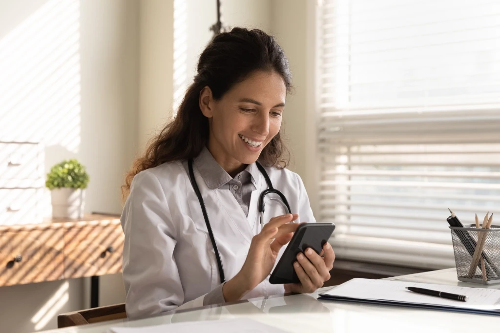 Ffemale doctor sitting at her desk checking her phone.