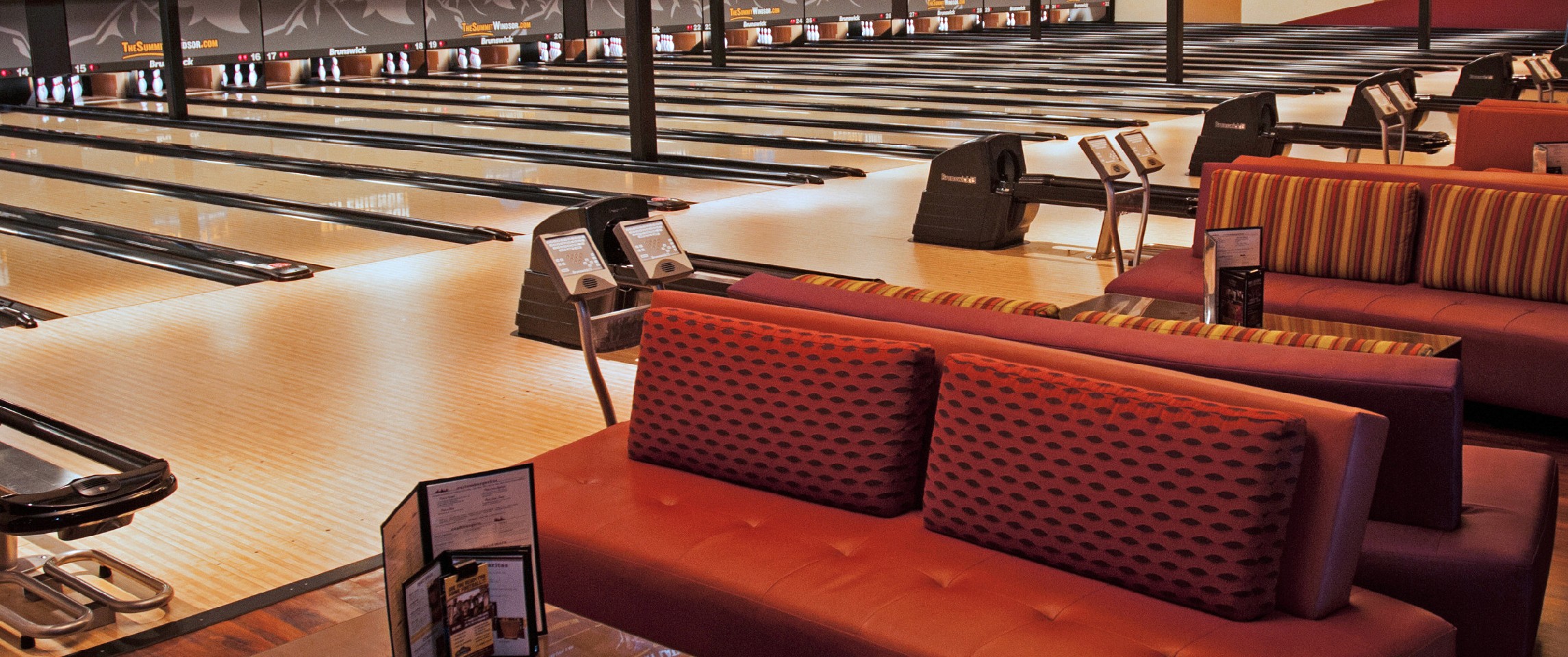 A young person with curly hair smiles at the camera while sitting in front of a laptop against a dark background.