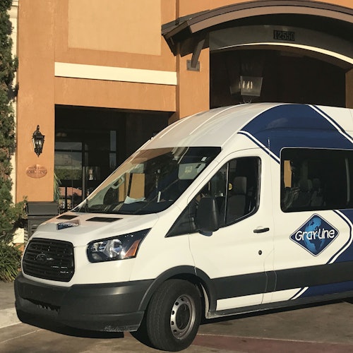 En vit skåpbil med "Gray Line"-reklam står parkerad framför en byggnad med en stor bågformad entré och nummer 12655.