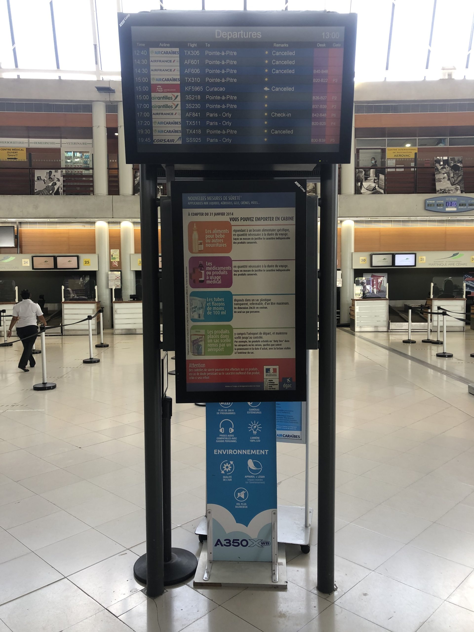 Écran des départs de l'aéroport affichant plusieurs annulations de vols, avec les informations d'enregistrement et les avis de sécurité ci-dessous. Le terminal est presque vide.