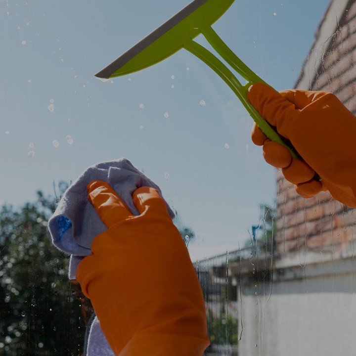 une femme avec des gants oranges nettoie une vitre