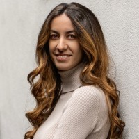 Frontalbild einer jungen Frau, die über die Schulte in die Kamera lächelt.