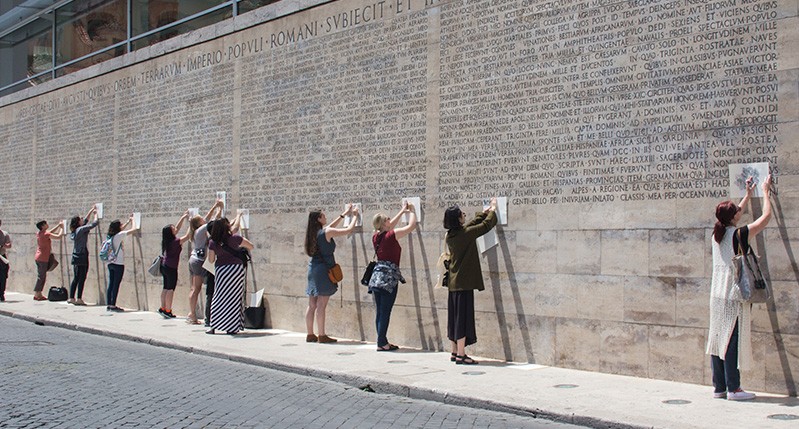 people making frottage on letters on roman wall