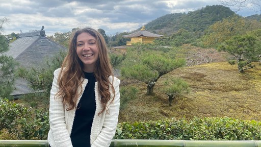 Woman smiling outdoors with rolling green hills in the background.