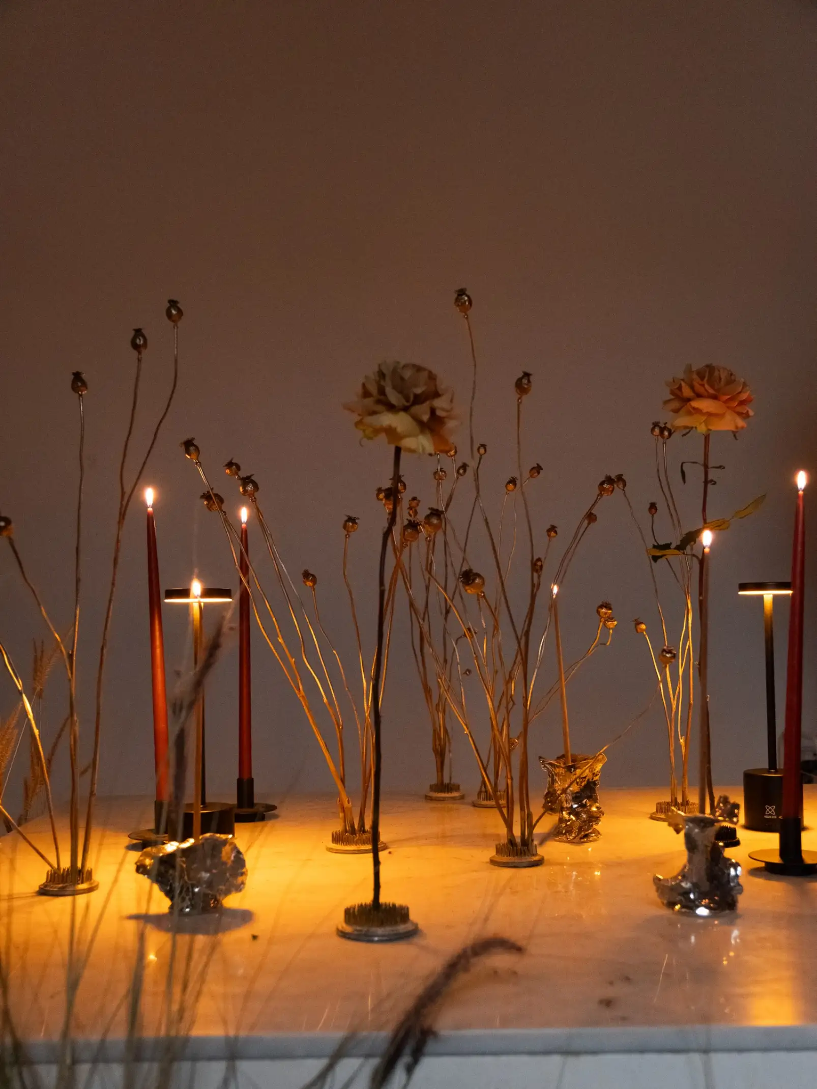 Instalación de velas y flores doradas sobre superficie iluminada para intervención artística, logrando un efecto etéreo y ceremonial.