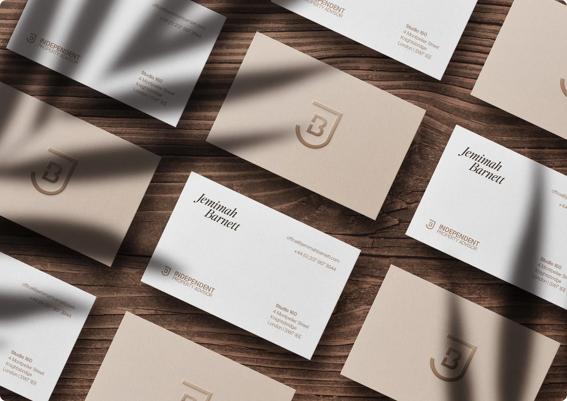 Top-down view of elegant cream and white business cards for “Jemimah Barnett” on dark wood, with logo details, soft shadows, and a refined tone.