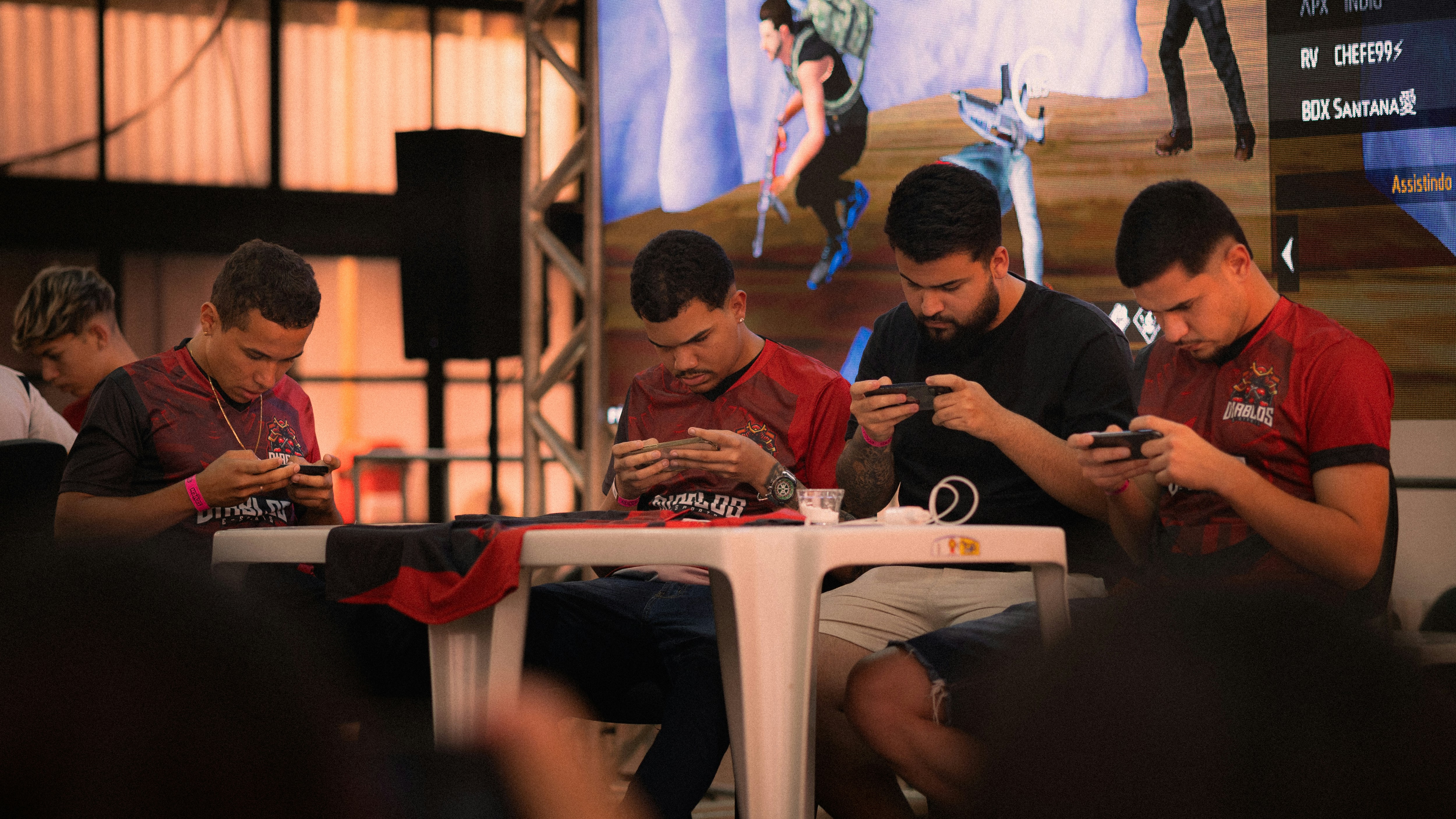 Four men playing mobile games at a table.
