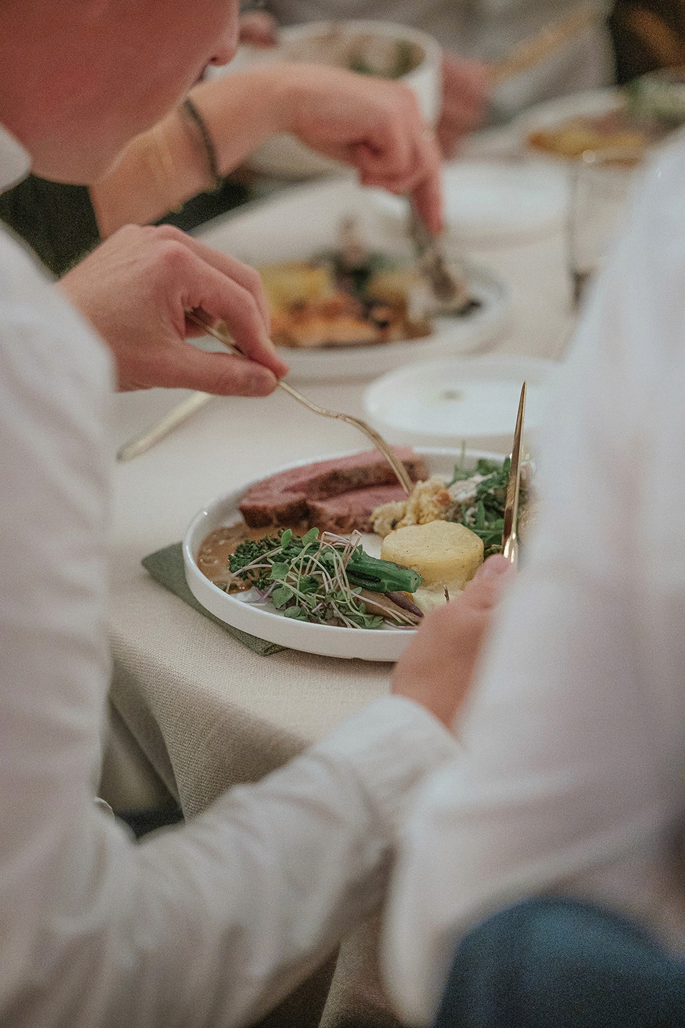Person wearing a beige apron whisking green matcha tea in a ceramic bowl on a kitchen counter.