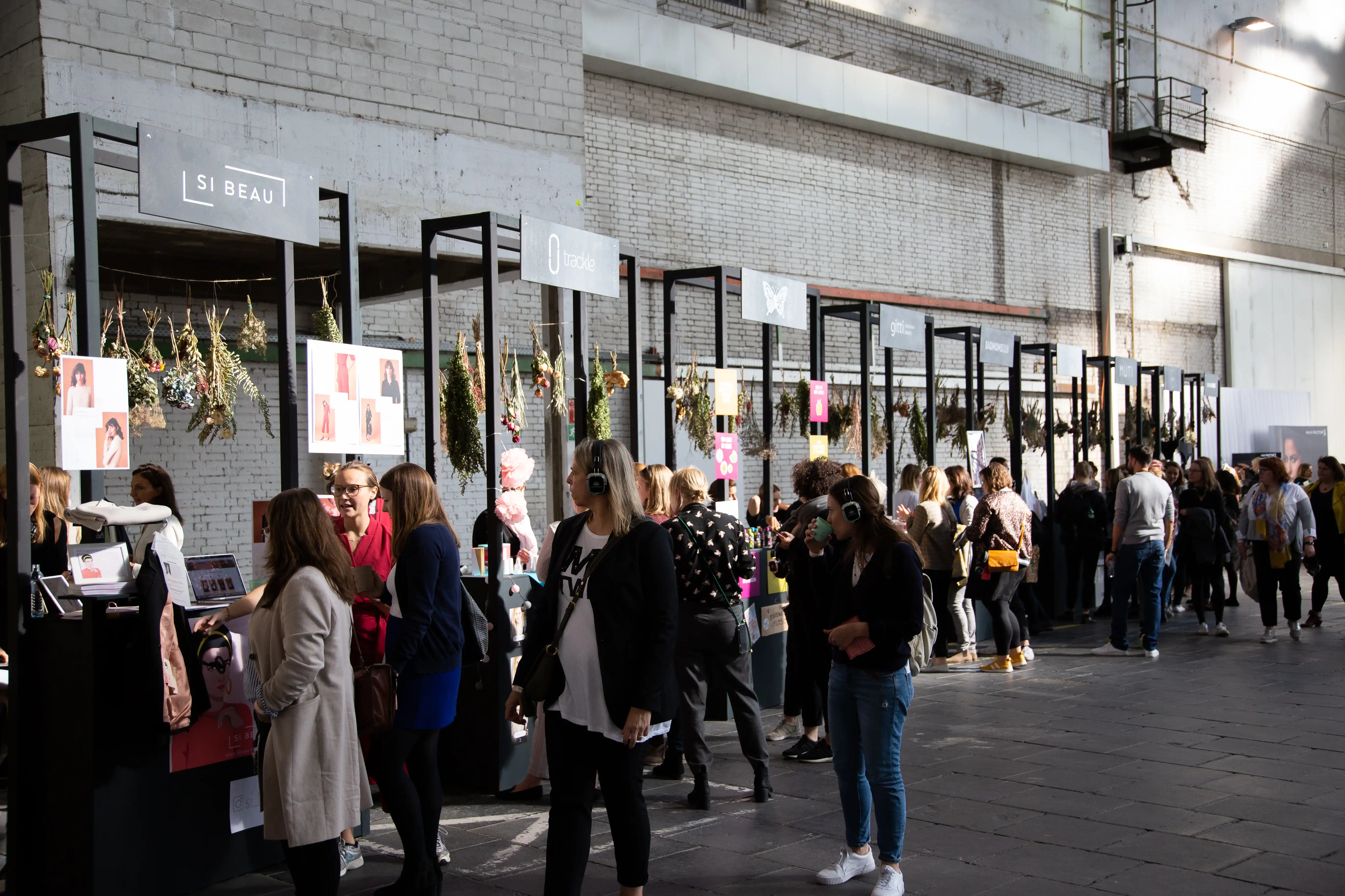 Visitors browsing brand stands with hanging dried-flower decor along the brick wall of the hangar at Female Future Force Day.