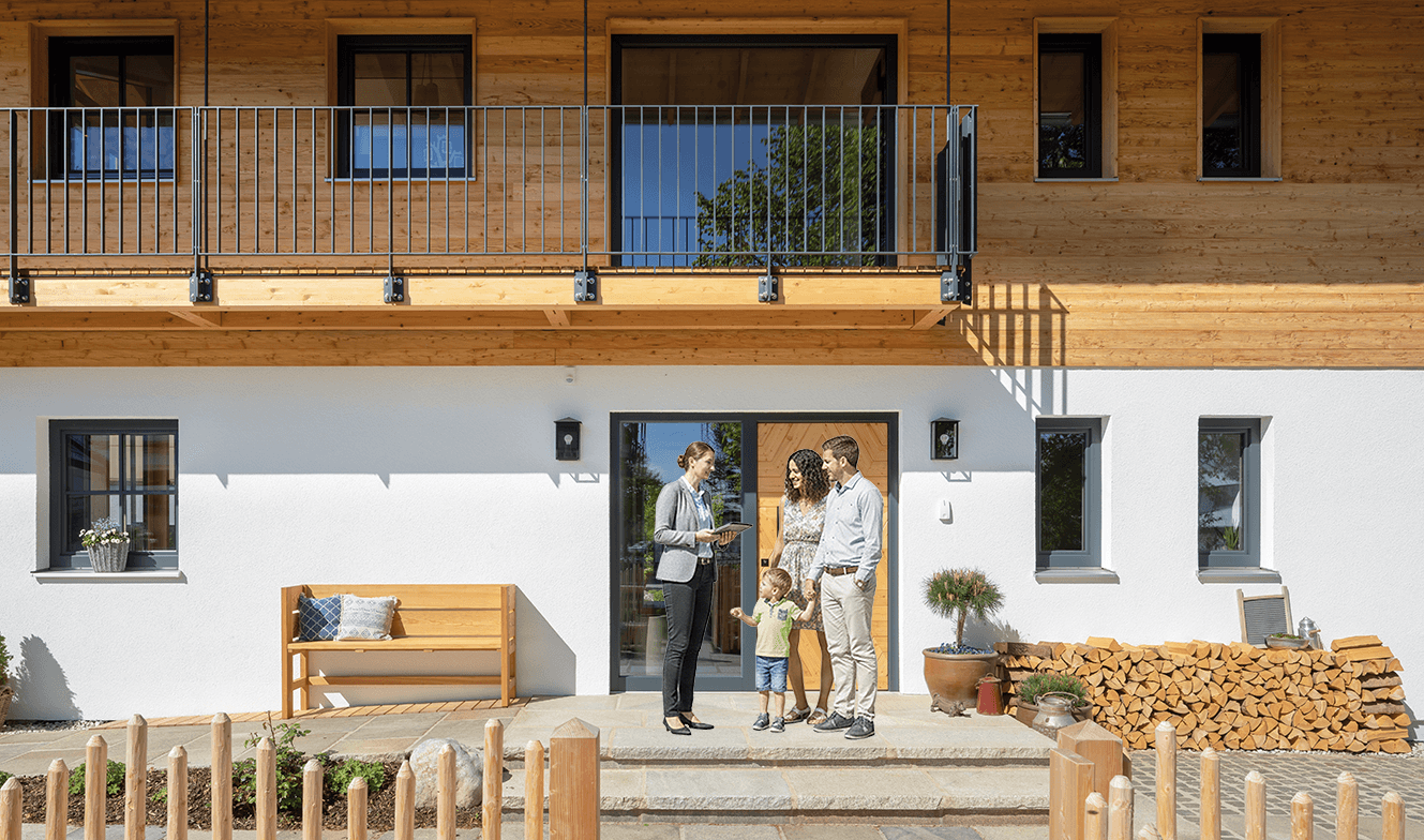 Immobilienmaklerin präsentiert ein Haus, das eine Familie mit lebhaftem Kind vor dem Eingang begrüßt.