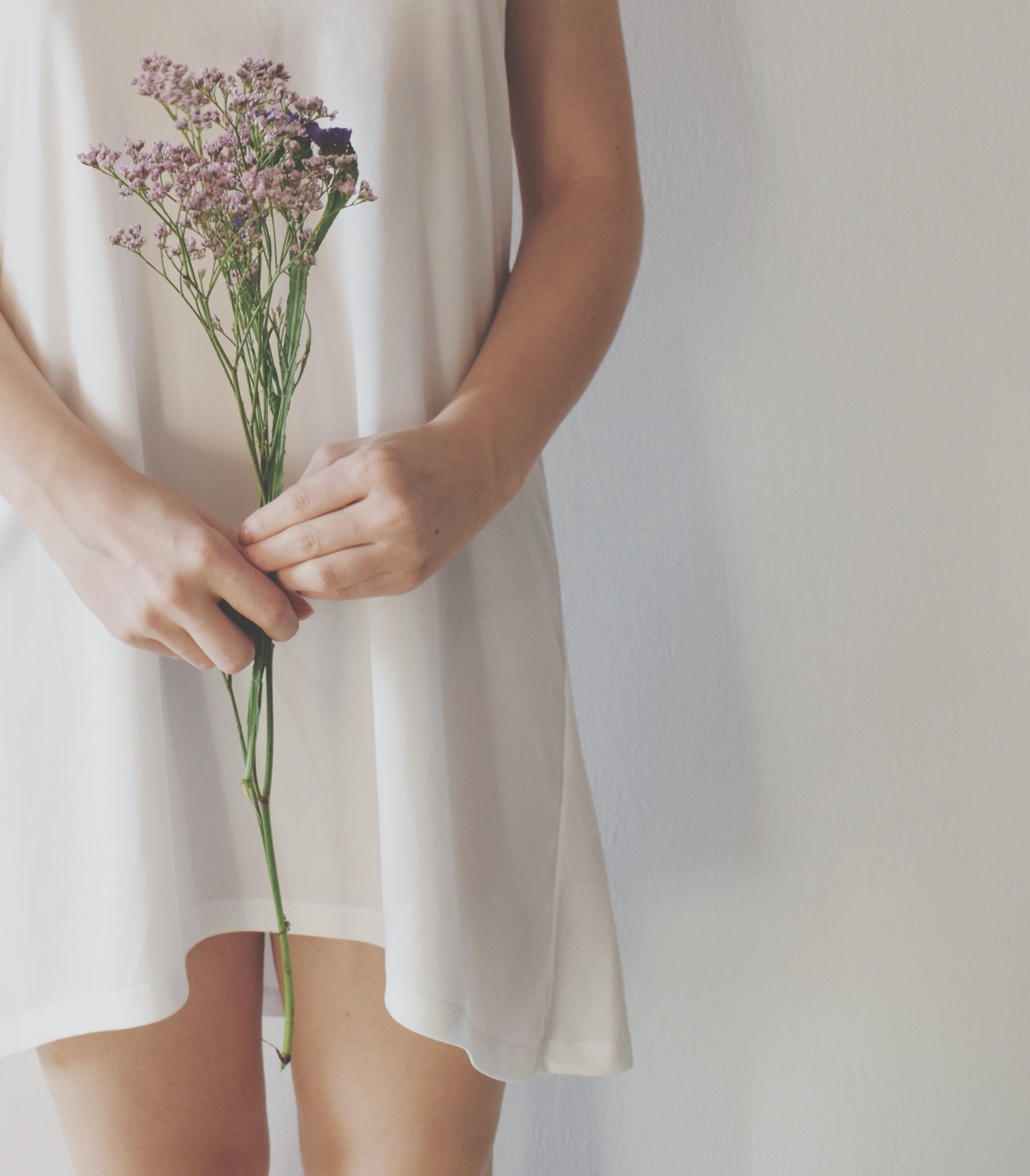 Vrouw in witte jurk houdt een bosje bloemen vast, symbool voor een uitblijvende cyclus en onvervulde kinderwens.