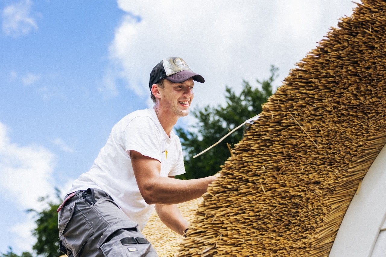 Rietdekker op het dak aan het werk van Rietdekkersbedrijf van Dijk