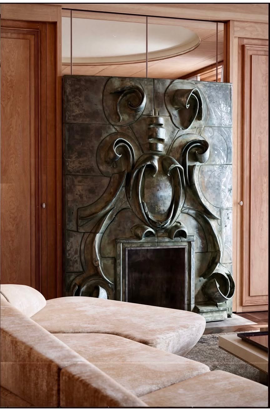 Living room with a sculptural metal fireplace, curved cream sofa, and mirrored wall.