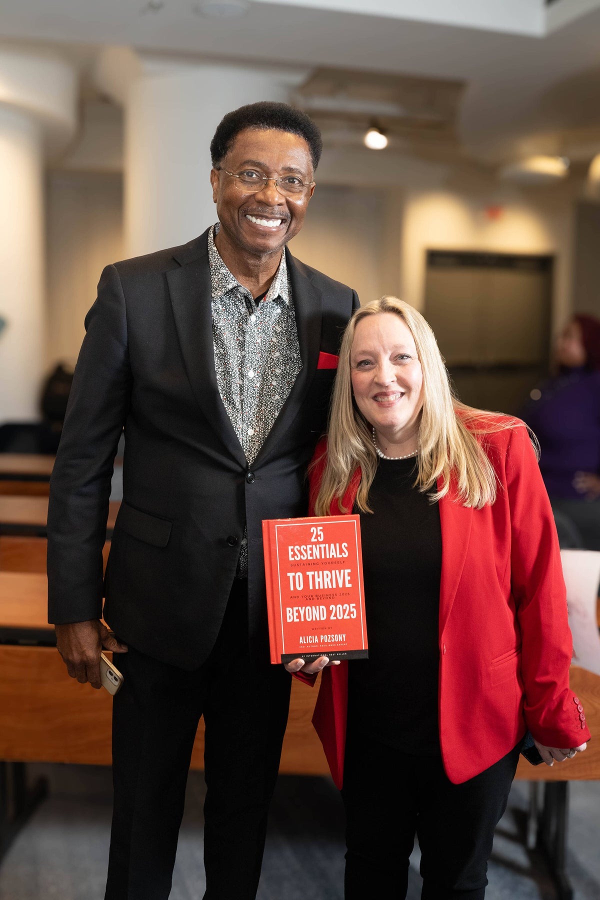 Alicia Pozsony poses with an event attendee while holding her book, 25 Essentials to Thrive Beyond 2025.